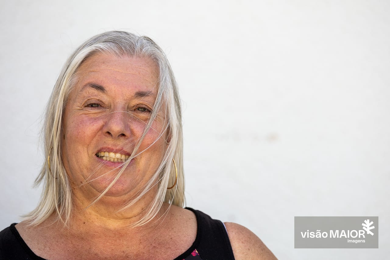 Mulher de cabelos brancos e brincos a olhar de frente para a câmara
