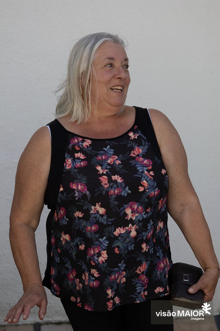 Mulher de cabelos brancos, brincos e camisa às flores a olhar de lado