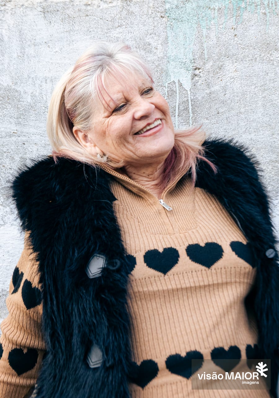 Mulher de cabelo claro e cabeça inclinada com um colete de pelo e camisola beje com corações