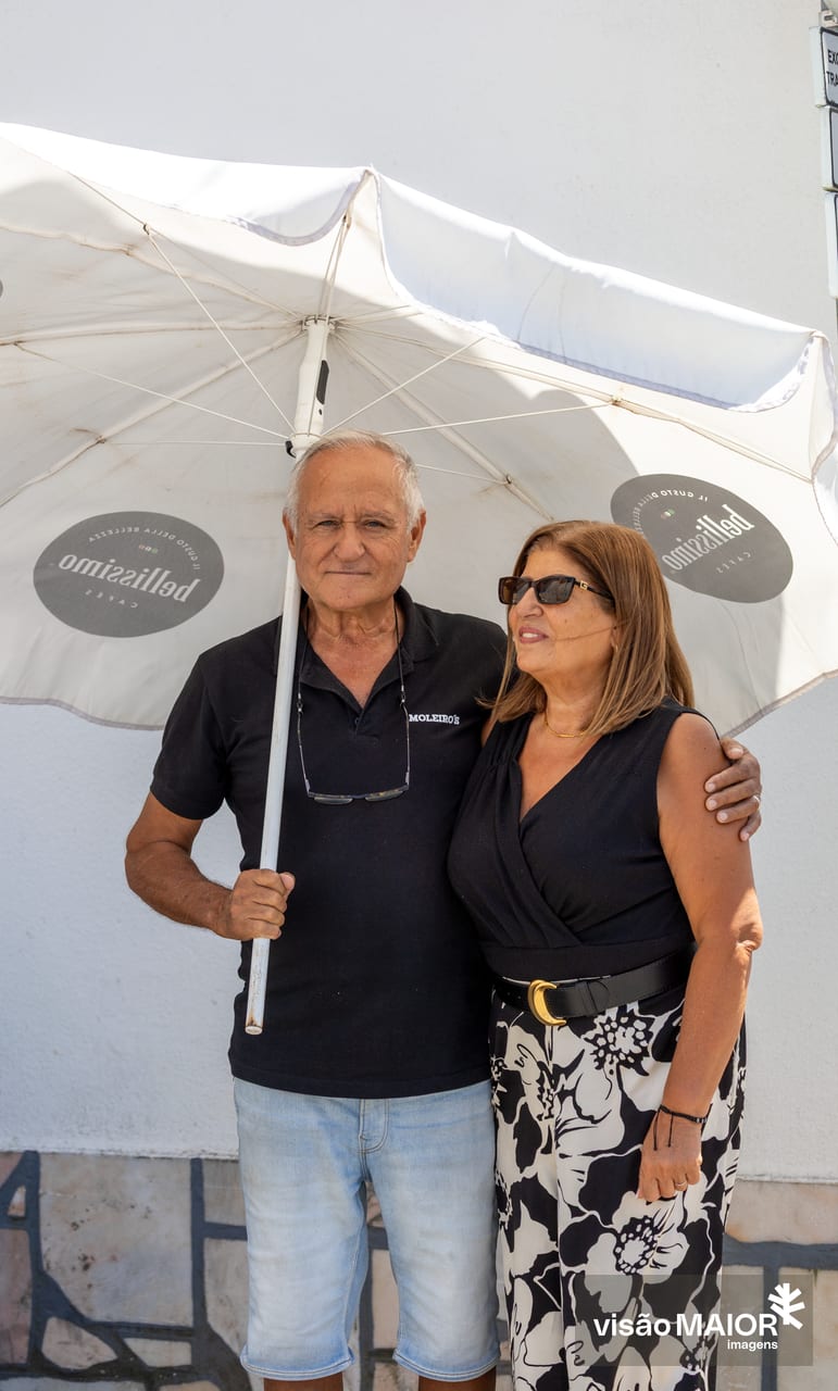 Casal em harmonia debaixo de um guarda sol, ele com a mão em cima do ombro dela