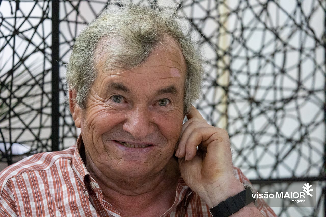 Homem de cabelo grisalho a rir, com a mão no ouvido, de relógio