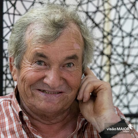 Homem de cabelo grisalho a rir, com a mão no ouvido, de relógio