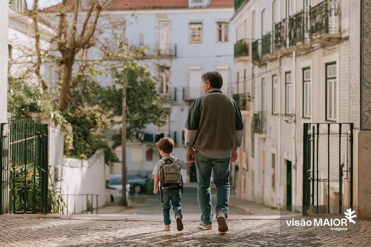 Imagem ferada com IA - Homen com criança pela mão, ambos de costas. A criança leva uma mochila às costas